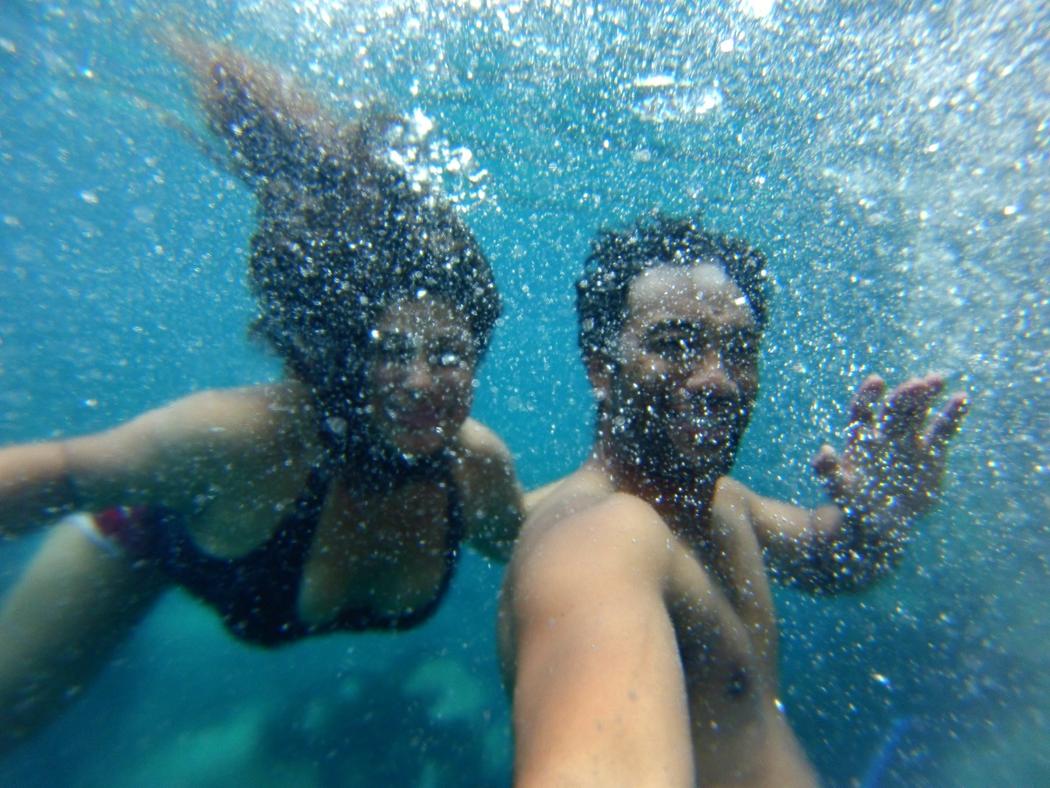 An underwater photo of two people smiling and waving happily with bubbles everywhere